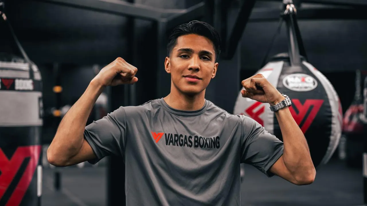 Athlete flexing in a Vargas Boxing shirt between heavy bags.